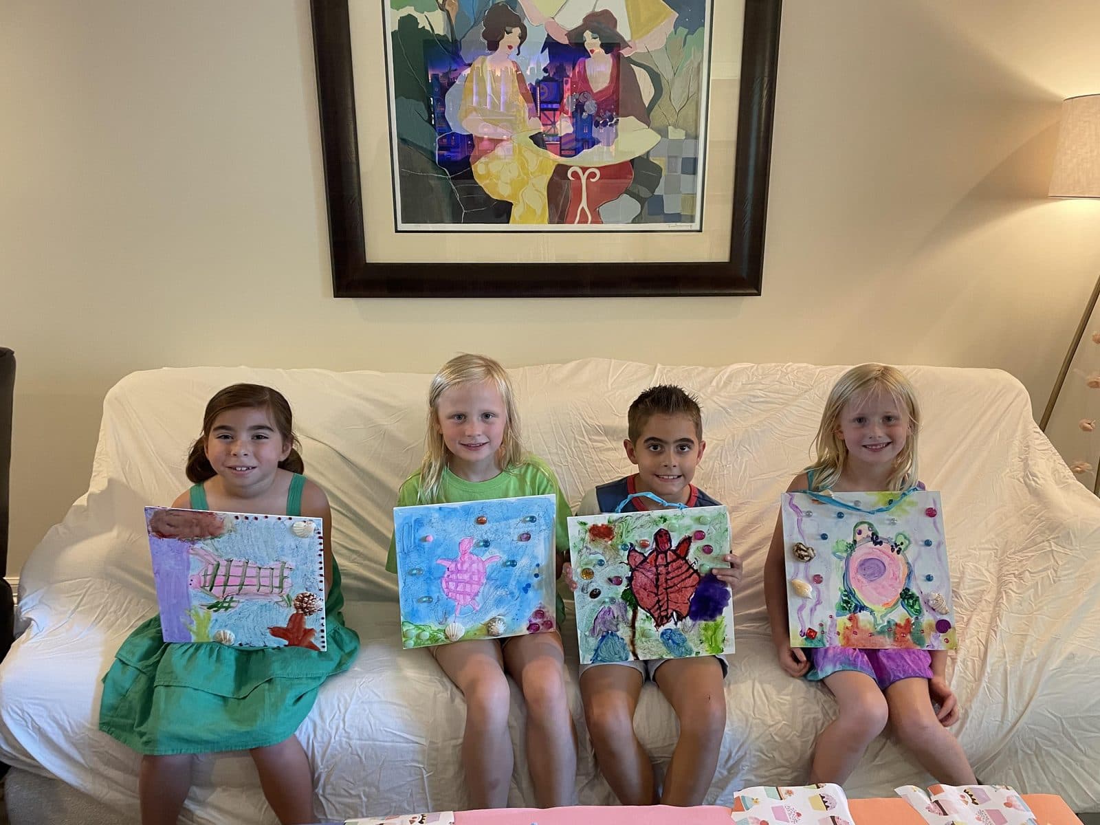 Four young artists on the studio couch, each proudly holding their finished painting